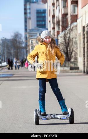 Junge kaukasische Mädchen tragen gelbe Jacke stehend auf Selbst-motiviert gyroscooter auf Urban Street Stockfoto