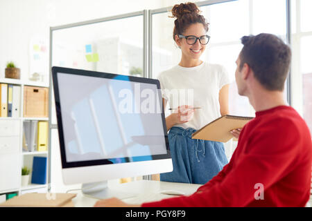 Zwei junge kreative Fachleute in Diskussion über ihre Ideen durch Computer Monitor im Büro Stockfoto