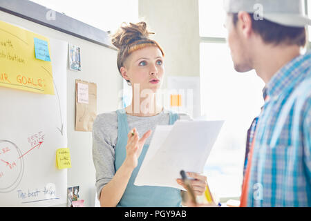 Ernsthafte unternehmungslustige weibliche Marketingspezialisten mit hipster Frisur erklären Daten und Gestik der Hand halten Marktanalyse mit Kollege im Büro Stockfoto