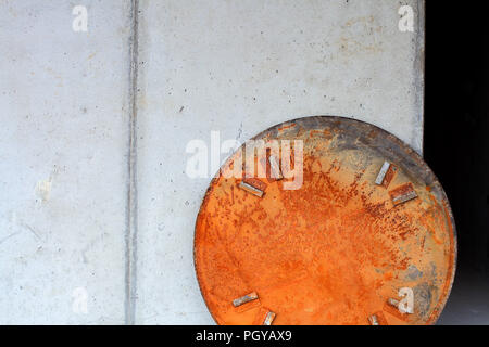 Rusty Kreis Abdeckung vor einer Betonwand Stockfoto