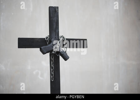 Schwarzes Kreuz mit Kette und Pistole auf Weiß grunge Wand. Objekt und Waffe Konzept. Christliche Religion Thema. Halloween und kriminellen Thema. Platz kopieren Stockfoto