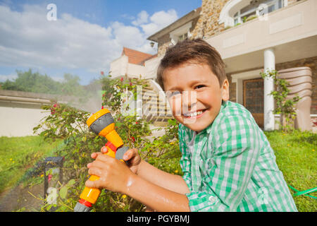 Close-up Portrait von Happy Boy Bewässerung Garten mit Sprinklerschutz im Sommer Stockfoto