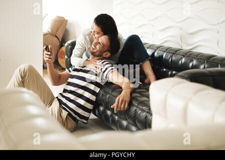 Happy Hispanic Paar mit Smartphones auf der Couch zu Hause Stockfoto