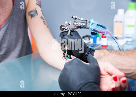 Close-up in die Hände eines erfahrenen Tätowierer mit schwarzen Handschuhen, während Sie einen sterilen Maschine für das Tätowieren in einem modernen Studio Stockfoto