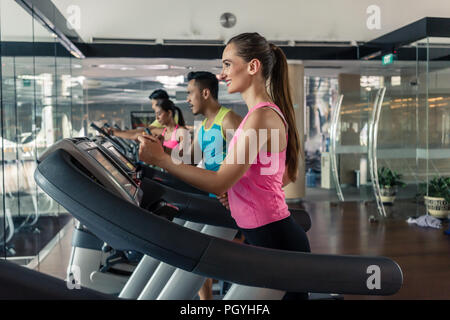 Fröhliche schöne Frau mit einem gesunden Lebensstil Trinkwasser während der Ausbildung auf dem Laufband in einer trendigen Fitness Club Stockfoto