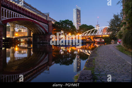 Manchester, England, UK - 30. Juni 2018: Hausboote bis Licht in Castlefield Becken in der Abenddämmerung auf Manchester City Centre fällt, mit einem Metrolink tram passi Stockfoto