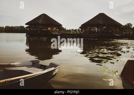 Bungalow mit Strohdächern auf dem See vor dem Hintergrund der Boote und Lilien im Sommer Stockfoto