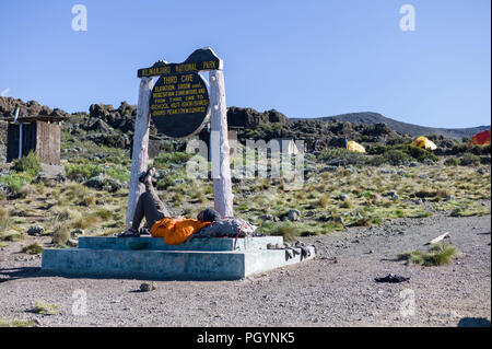 Wanderer ruhen auf Zeichen für Dritte Höhle Camp, Rongai Route, Kilimanjaro, Kilimanjaro, Tansania. Stockfoto