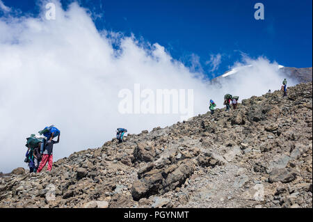 Torhüter tragen Lasten zum Barafu Camp auf der Machame Route mit Kibo Gipfel im Hintergrund, Kilimanjaro, Kilimanjaro, Tansania. Stockfoto