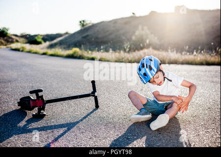 Wenig Sport kid Holding sein Knie leiden unter Schmerzen nach Unfall Roller Stockfoto