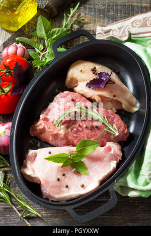 Frisches rohes Fleisch. Verschiedene Arten von rohem Schweinefleisch, Hühnchen und Rindfleisch mit Gemüse und Kräutern auf Holztisch. Stockfoto