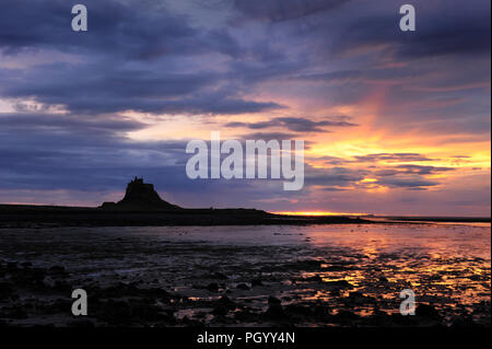 Lindisfarne Castle, der heiligen Insel, in der Morgendämmerung, als die Sonne gesehen erhebt sich über der Nordsee und Ebbe in der Lindisfarne Hafen, Northumberland. Stockfoto