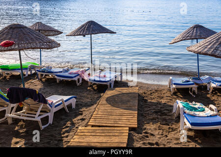 Einen leeren Strand in einem himmlischen Bucht. Sonnenschirme mit Liegen und Handtüchern auf Handtücher. Meer und Himmel Hintergrund. Stockfoto