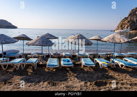 Einen leeren Strand in einem himmlischen Bucht. Sonnenschirme mit Liegen und Handtüchern auf Handtücher. Meer und Himmel Hintergrund. Stockfoto