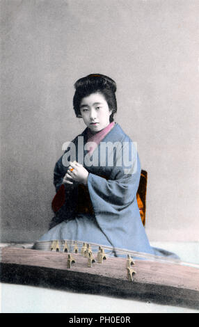 [1910s Japan - Frau im Kimono Spielen der Koto] - junge japanische Frau im Kimono und traditionelle Frisur Spielen der Koto, einem traditionellen japanischen Saiteninstrumente Musikinstrumente. 20. jahrhundert alte Ansichtskarte. Stockfoto