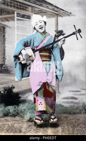 [1910s Japan - die blinde Frau Spielmann] - junge japanische Frau im Kimono und traditionellen Kopfbedeckungen, Singen und Spielen die Shamisen, eine 3-saitige Instrument gespielt mit einem bachi (plektrum). 20. jahrhundert alte Ansichtskarte. Stockfoto