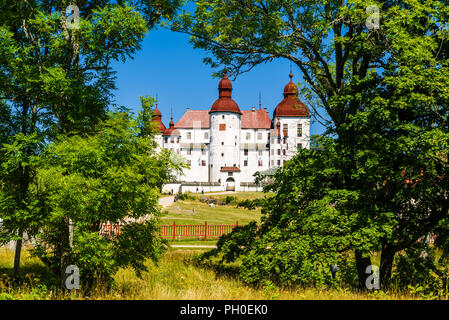 Lidkoping, Schweden - 4. Juli 2018: Lacko Schloss durch den Vordächern von einigen Bäumen an einem sonnigen Sommertag gesehen. Touristen Wandern auf einem Weg außerhalb des c Stockfoto