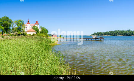 Eine leere Badesteg am See Vanern mit im Vordergrund Schilfrohr und Lacko Schloss im Hintergrund. Lage Lacko außerhalb Lidkoping in Schweden. Stockfoto