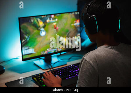 Bild von eingetaucht teenage Gamer junge Videospiele auf Computer im dunklen Zimmer Kopfhörer tragen und mit bunten Tastatur mit Hintergrundbeleuchtung Stockfoto