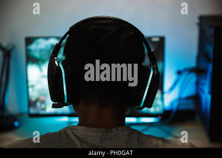 Ansicht von Hinten Nahaufnahme der jungen Gamer Junge spielt Videospiele online am Computer in dunklen Raum Kopfhörer mit Mikrofon Stockfoto