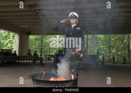 BANGOR, Washington (14. Juni 2018) Chief Hospital Corpsman Farrah Ocasio, aus Detroit, Michigan, Trident Training Service in Bangor, Washington zugewiesen, macht ein Gruß nach Platzieren der Überreste einer US-Flagge zu einem Brand während einer Flagge in den Ruhestand Zeremonie am Marinestützpunkt Kitsap-Bangor. Wenn eine US-Flagge abgenutzt, zerrissen, blasse oder stark verschmutzt, sollte es mit der Würde und Achtung, die es in den Ruhestand versetzt. BANGOR, Washington (14. Juni 2018) Musiker 1. Klasse Chris Hodges, von Tuscaloosa, Alabama, zur Marine Band Nordwesten zugeordnet, die Trompete spielt, während eine Flagge in den Ruhestand Zeremonie am Marinestützpunkt Kitsa Stockfoto