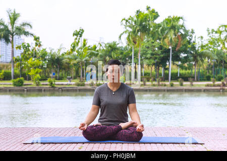 Gesunde asiatische Frau mittleren Alters yoga Lotus im Stadtpark am Morgen dar. gesund und Lifestyle Konzept. Stockfoto