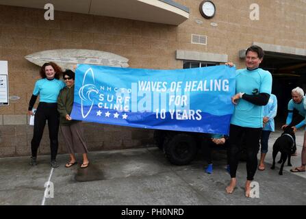 DEL MAR, Kalifornien (14. Juni 2018) Naval Medical Center San Diego (NMCSD) Surf Klinik Mitarbeiter und Freiwilligen präsentieren eine "Glückwunsch"-Banner zu Betty Michalewicz - Kragh, surf Therapie Programm Manager und Leistungsdiagnostiker bei Gesundheits- und Wellness- Abteilung, während der 10-Jahr-Feier des Surf Klinik. Die Surf Klinik ist vom Gesundheits- und Wellness- Abteilung koordiniert, Verwundete, Kranke zu rehabilitieren, und verletzten Service Mitglieder durch Übung und entspannende Therapie zur Verbesserung ihrer körperlichen, geistigen und sozialen Wohlbefindens. Stockfoto