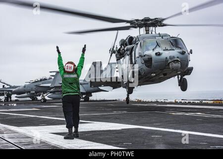 Pazifik (20. Juni 2018) Flieger Yulisa Hernandez Garcia leitet die Crew von einem MH-60S Sea Hawk Hubschrauber zum "Schwarzen Ritter" der Hubschrauber Meer Combat Squadron (HSC) 4 zugewiesen, wie es braucht, um von der Flight Deck der Nimitz-Klasse Flugzeugträger USS Carl Vinson (CVN 70). Carl Vinson ist derzeit in der Vorbereitung für die Teilnahme an den Rand der Pazifischen Übung 2018 im Gange. Stockfoto