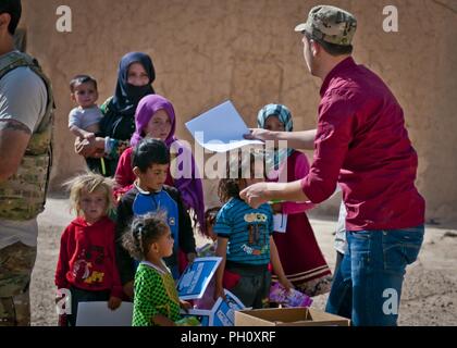 Ein Mitglied des Syrischen demokratischen Kräfte Hände Malbücher für Kinder in einem erst kürzlich befreiten Stadt, in der Nähe von Dashisha, Syrien, 17. Juni 2018. Die syrischen Demokratischen Kräfte, mit Unterstützung von ihren Koalitionspartnern, sind aktiv in Betrieb Zusammenfassung, eine SDF-engagiert-geführten militärischen Offensive der letzten verbleibenden Taschen von ISIS Kämpfer in Syrien naher Fluss Euphrat Valley zu beseitigen. Stockfoto