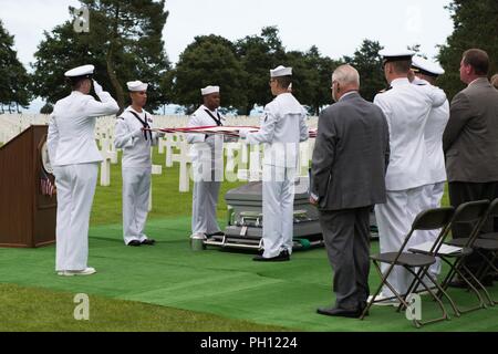 Normandie, Frankreich (19. Juni 2018) Die U.S. Naval Hospital Neapel Ehrengarde hält die amerikanische Flagge über die Überreste von Radioman 2. Klasse Julius "Henry" Pieper als "Hähne" wird während einer Trauerfeier in der Normandie amerikanische Friedhof gespielt. Henry Pieper und seinem Zwillingsbruder, Radioman 2. Klasse Ludwig "Louie" Pieper, waren beide getötet, als ihr Schiff, Landing Ship Tank (LST) 523, schlug eine vor der Küste von Frankreich am 19. Juni 1944. Louie's Überreste wurden sofort gefunden, aber Henry's Überreste wurden nicht bis Dezember 2017 identifiziert. Die Familie beantragt, dass Henry in der Normandie n begraben werden. Stockfoto
