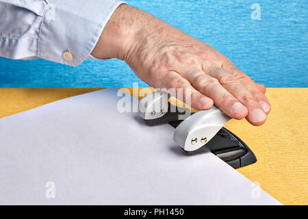 Hand macht Löcher in Papier mit einem Büro von Lochungen. Stockfoto