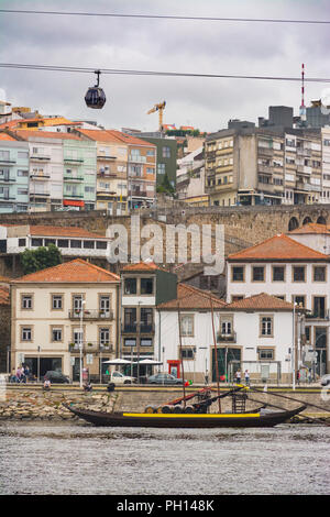 Seilbahn über die Lagerhäuser und Keller von Gaia, mit einem traditionellen Weinhandelsboot, das auf dem Douro Fluss festgemacht ist. Porto, Portugal Stockfoto