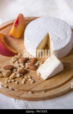 Weiß köstliche hausgemachte camambert Käse auf einem Holzteller serviert mit Mandeln, Cashew, Pinienkernen und Pfirsich. Dessert für ein Abendessen mit der Familie. Brie. Stockfoto