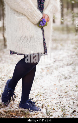 Schönen Schneeglöckchen in die Hände einer jungen Frau in Weiß Strickjacke und Blues flower Dress. Erste Frühling Blumen in einem Wald. Anfang des Frühlings. Prepar Stockfoto