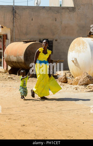 Weg zum Kalvarienberg, SENEGAL - 23.April 2017: Unbekannter senegalesische Frau im gelben Kleid geht mit einem kleinen Mädchen. Noch viele Menschen im Senegal leben in Stockfoto