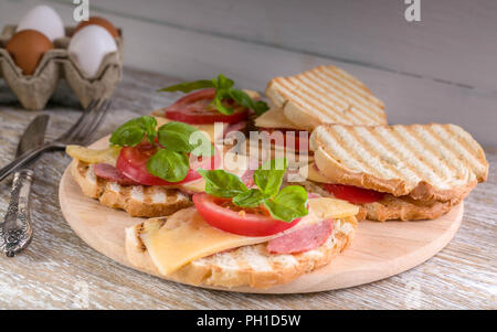 Belegte Brötchen mit Wurst, Käse, Tomaten und Basilikum Stockfoto