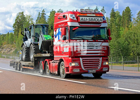 Orivesi, Finnland - 27. August 2018: DAF XF Truck von Ali-Simola Transporte landwirtschaftlichen Schlepper auf Schwanenhals trailer entlang nasse Autobahn an einem regnerischen Tag. Stockfoto