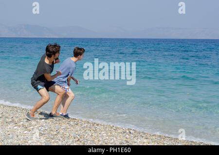 Zwei Brüder sind skimming Steine auf dem Wasser Spaß am Strand zu haben. Stockfoto