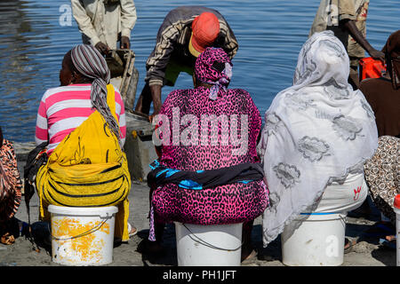 SAINT LOUIS, SENEGAL - Apr 24, 2017: Unbekannter senegalesischen Frauen in bunten Gewändern sitzen auf den Eimer in den Hafen von Saint Louis, einer Der bigges Stockfoto