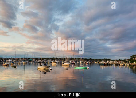 Die aufgehende Sonne bringt Farbe zu dramatischen Wolken über Sonnenbeschienene Boote im Hafen kurz nach Sonnenaufgang in Falmouth, Massachusetts auf Martha's Vineyard. Stockfoto