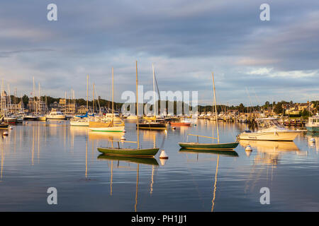 Die aufgehende Sonne bringt Farbe zu dramatischen Wolken über Sonnenbeschienene Boote im Hafen kurz nach Sonnenaufgang in Falmouth, Massachusetts auf Martha's Vineyard. Stockfoto