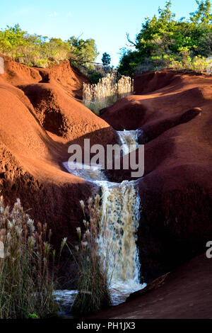 Ein Wasserfall schlängelt sich durch die rote Erde in der Nähe von Waimea Canyon, Kauai, Hawaii, USA. Waimea ist Hawaiianisch für "ddish Wasser." Stockfoto