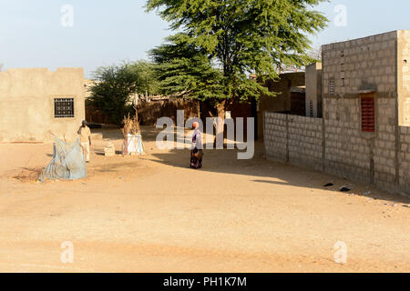 Weg zum Kalvarienberg, SENEGAL - 23.April 2017: Unbekannter senegalesische Frau in heller Kleidung und Kopftuch steht mit einer Tasche vor dem Baum. Noch Stockfoto