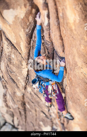 Weibliche Kletterer baumelt von der Kante einer anspruchsvollen Klippe. Stockfoto