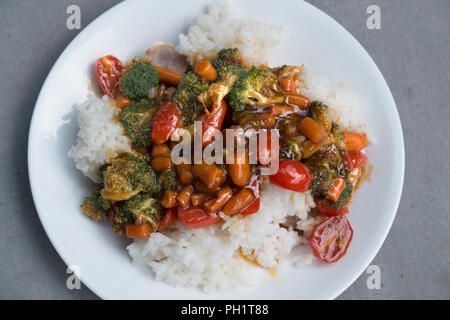 Gemüse Rühren braten mit Brokkoli, Karotten und Tomaten auf weißem serviert, Langkornreis. Stockfoto