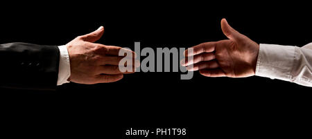 Zwei Männer, die sich die Hände zu schütteln, einer in einem Anzug und den anderen in seiner shirtsleeves über einen dunklen Hintergrund. Stockfoto