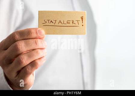 Close up einfach wachsam bleiben Konzept Design mit Geschäftsmann mit kleinen Holzschild mit Unterstrichenen bleiben Sie wachsam Texte über Weißen Hemd. Stockfoto