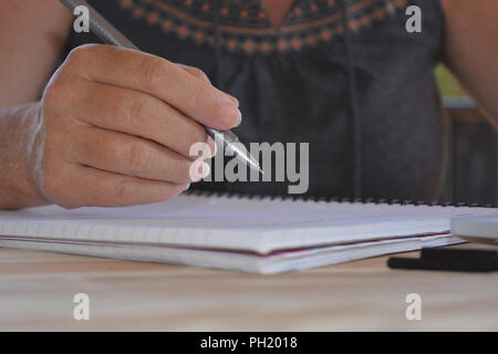 Frau an einem hölzernen Tisch pen balanciert, bereit in ein Notizbuch zu schreiben sitzt. Selektiver Fokus auf Pen nib, mit kopieren. Stockfoto