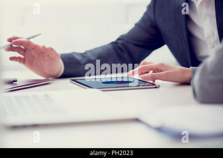 Retro Image der männlichen und weiblichen Geschäftspartnern Überprüfung der statistischen Diagrammen auf eine digitale Tafel sitzt in einem hellen Büro am weißen Schreibtisch. Stockfoto