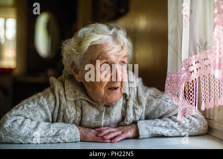 Grauhaarige ältere Frau sitzt und schaut aus dem Fenster. Stockfoto